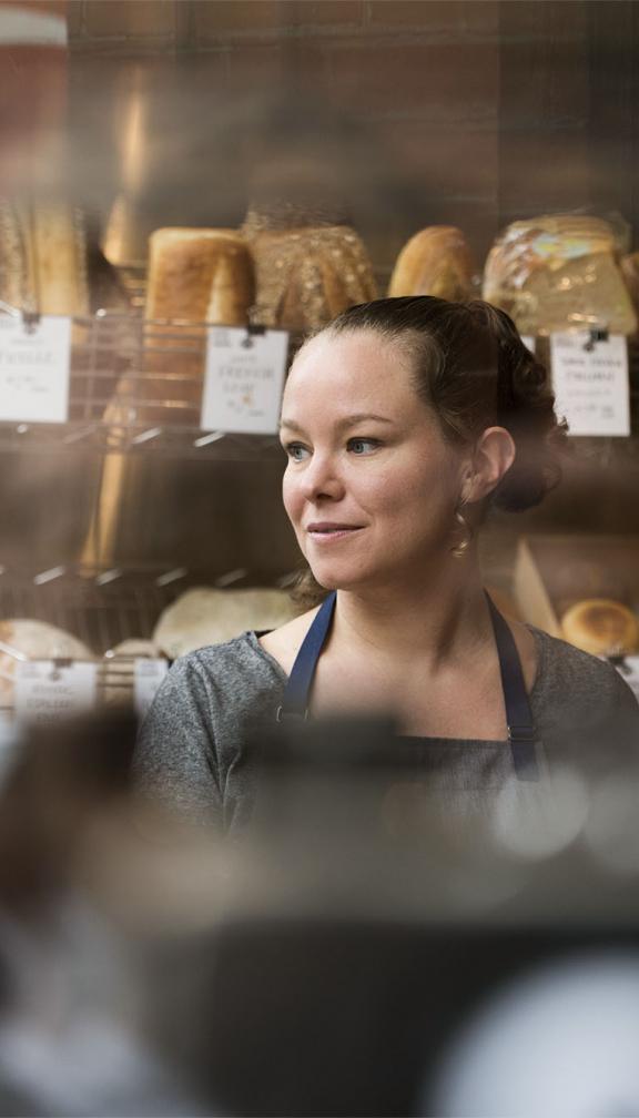 Woman standing in bakery with apron in front of freshly made bread
